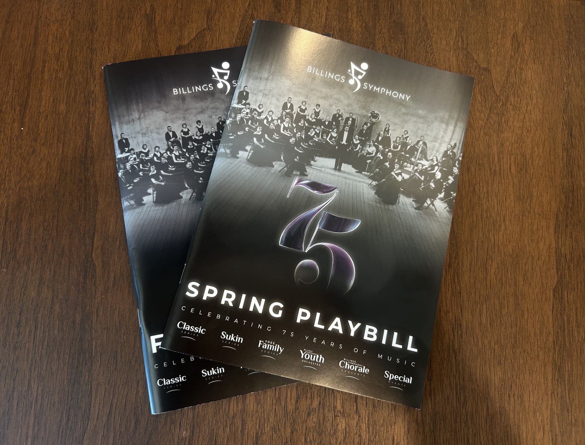 Two overlapping Billings Symphony playbills on a wooden table, showing 'SPRING PLAYBILL' on the front cover.