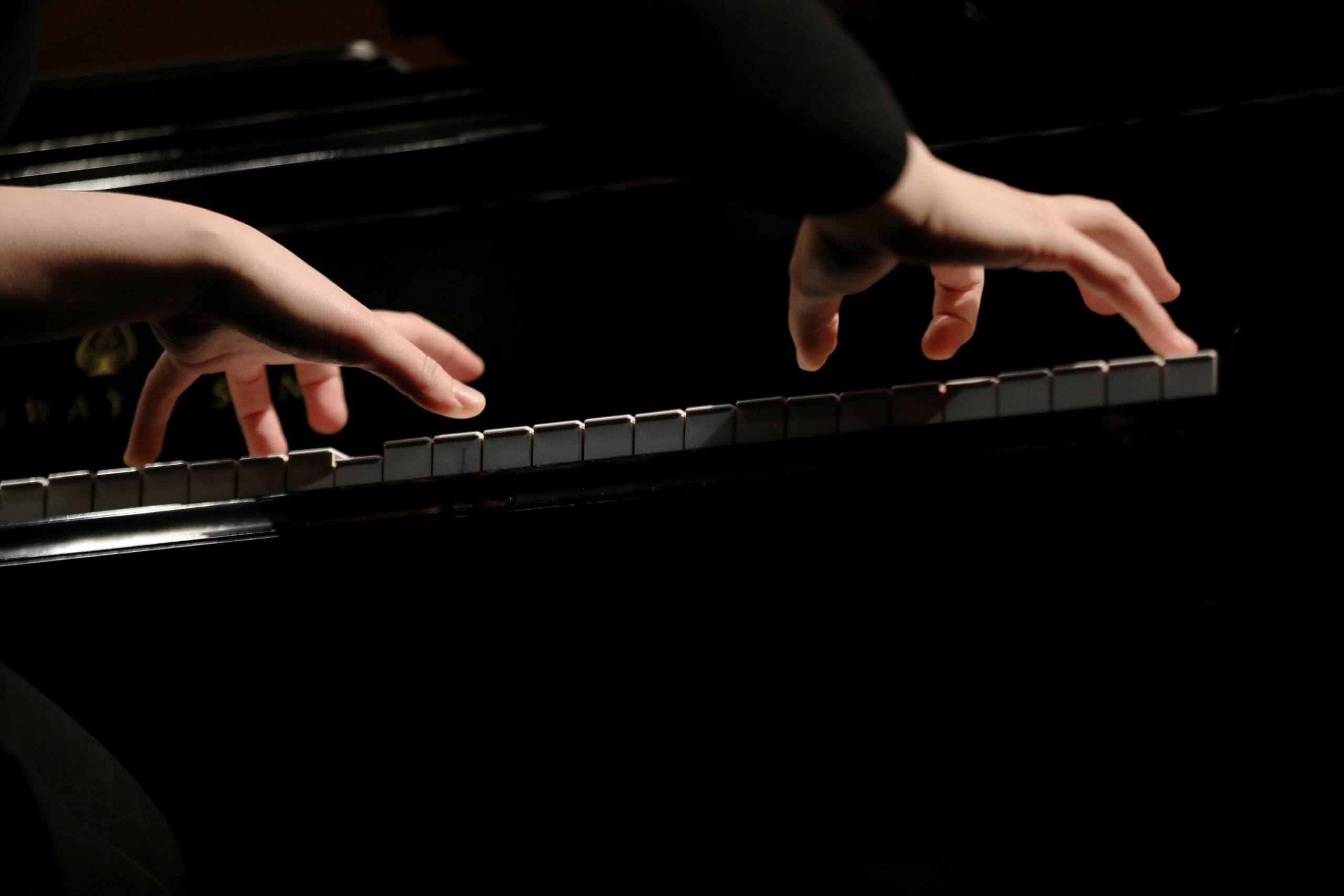 Close-up of hands playing a piano keyboard in dim lighting.